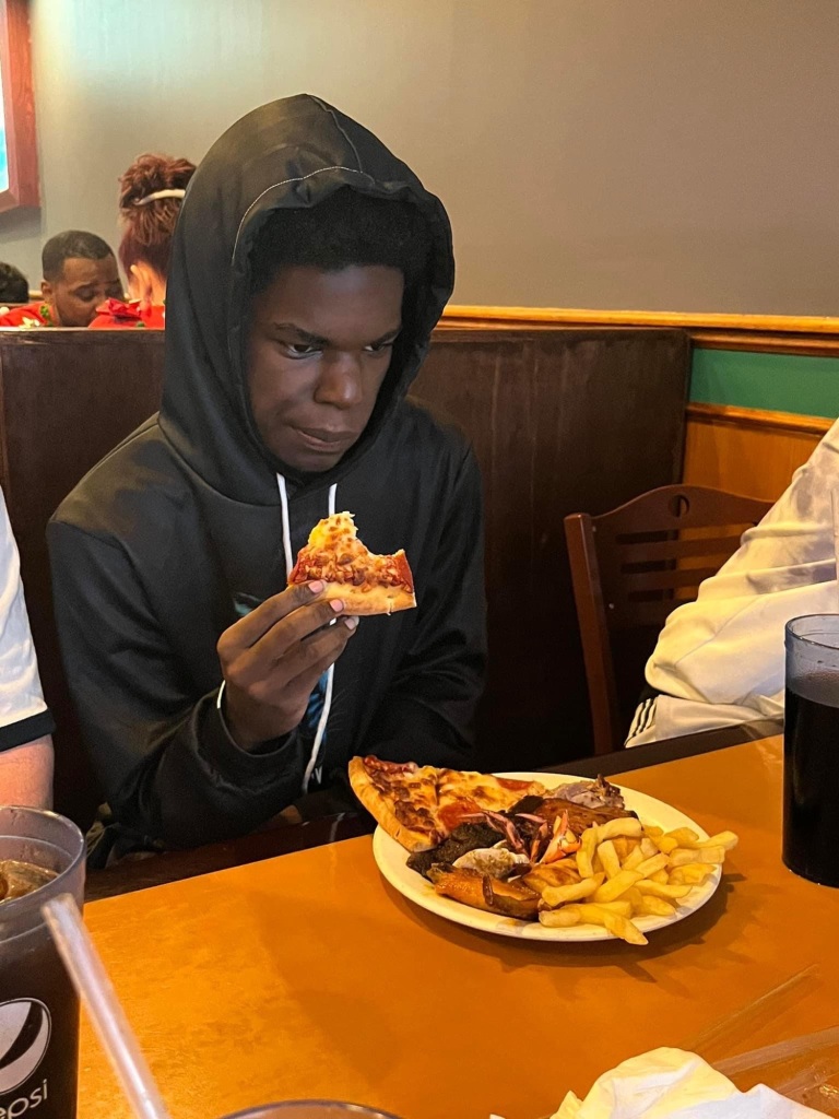 Teenage boy in a hoodie eating pizza.