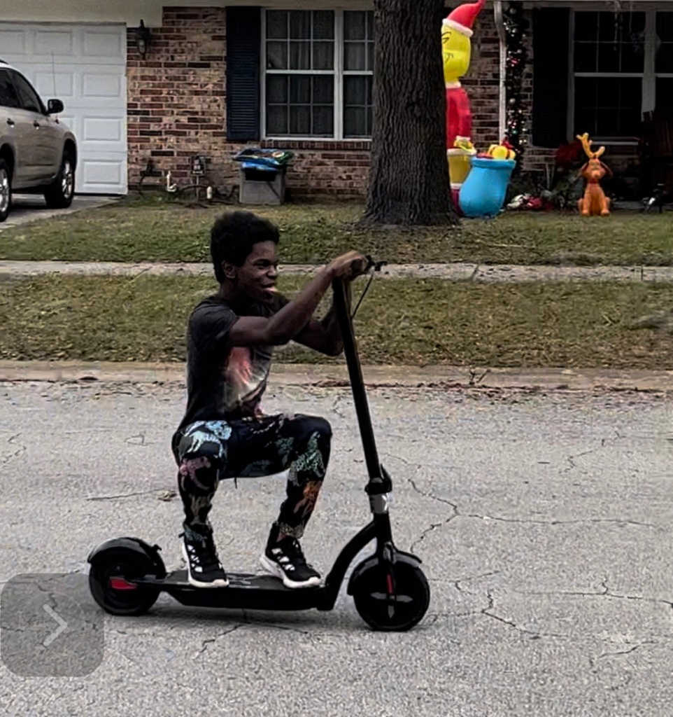 16 year old African American boy riding an electric scooter.